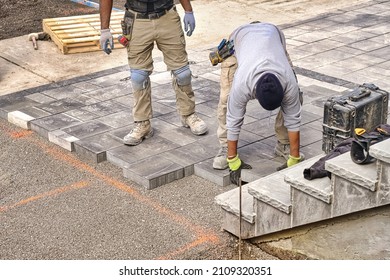 Construction workers wearing safety protective gear and working on high quality landscaping driveway pavement site. Contractors laying interlock patio with stone brick tile.