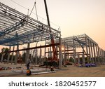 Construction workers are working at height above roof to instrallation accessory steel structure roof truss at construction site factory project during sunset time