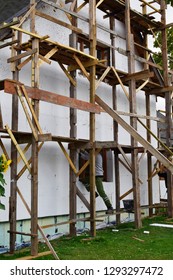 Construction Workers Working On Wooden Scaffolding Installing Polystyrene Foam Plates On Building Facade For House Insulation Outdoors In Summer. Home Improvement, Energy Saving And Diy Concept.
