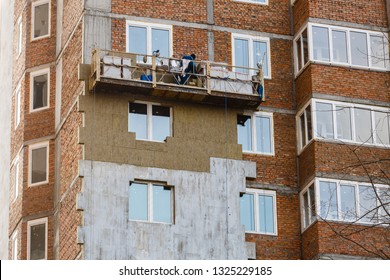 Construction Workers Working On Wooden Scaffolding Installing Polystyrene Foam Plates On Building Facade For House Insulation Outdoors In Summer. Home Improvement, Energy Saving And Diy Concept.