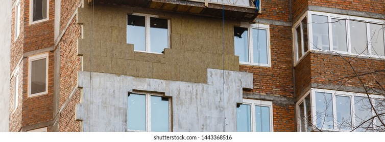 Construction Workers Working On Wooden Scaffolding Installing Polystyrene Foam Plates On Building Facade For House Insulation Outdoors In Summer. Home Improvement, Energy Saving And Diy Concept.