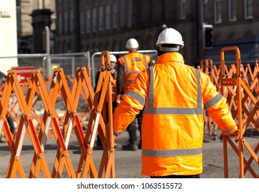 Construction/road Worker In Hi-Vis Gear And PPE Operating A Traffic Barrier On A City Street