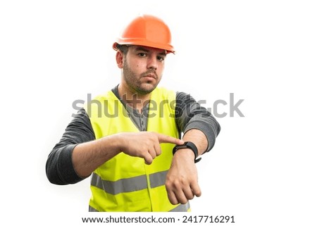 Constructor man wearing orange hardhat and florescent vest pointing index finger at smart watch on wrist as timekeeping concept isolated on white background