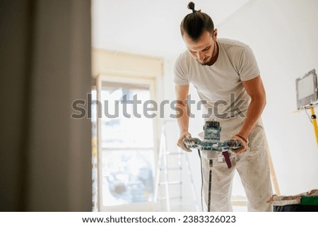 A constructor is mixing plaster with manual cement mixer while standing in an apartment in a renovation process. A house painter is mixing material for skim coating while renovating home. Copy space.