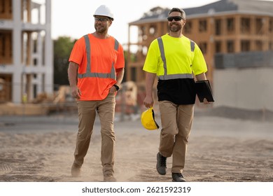 Constructors engineers in construction clothes walk along the construction site near an unfinished house through the dust. engineer and worker plan working for the outdoors building construction site