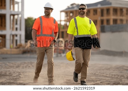 Constructors engineers in construction clothes walk along the construction site near an unfinished house through the dust. engineer and worker plan working for the outdoors building construction site