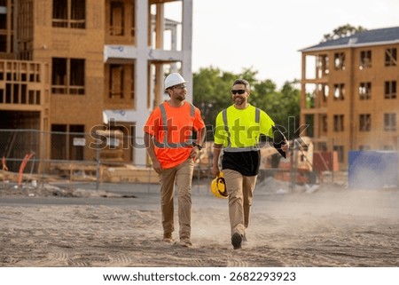 Constructors engineers in construction clothes walk along the construction site near an unfinished house through the dust. engineer and worker plan working for the outdoors building construction site