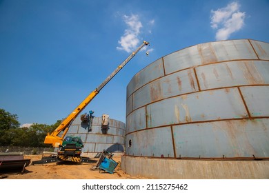 Constuction of an oil derrick crane, big oil tanks on the background.