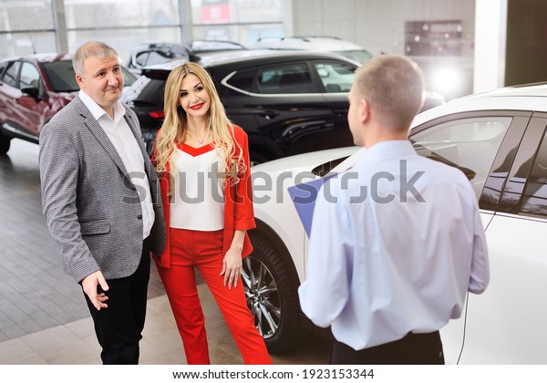 a consultant manager of a car salon or car shop with\
a tablet in his hands shows a couple new cars. A man and a woman\
choose a car.