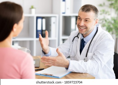 Consultation Concept. Portrait Of Smiling Male General Practitioner Doctor Talking To Female Patient During Appointment At His Office, Explaining Prescription. Therapist Sitting With Woman At Desk