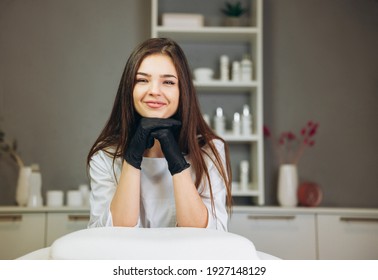 Consultation In Cosmetology Clinic. Female Beauty Doctor In White Coat And Black Gloves Smiles Nicely. Healthcare Concept.