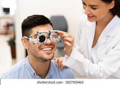 Consultation With The Ophthalmologist Concept. Portrait Of Woman Optometrist Examining Eyesight Of Male Client With Trial Frame And Closed Eye. Woman Doing Checkup Of Man's Eye With Diagnostic Tool