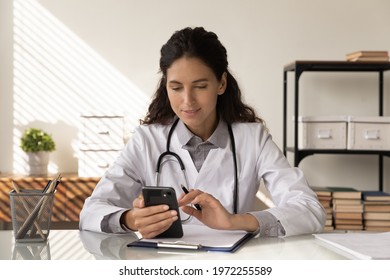 Consulting Patient By Internet. Focused Female Medic Sit At Workplace Hold Phone Text Message To Client Check Health Status On Distance. Woman Doctor Work With Smartphone Read Email From Sick Person