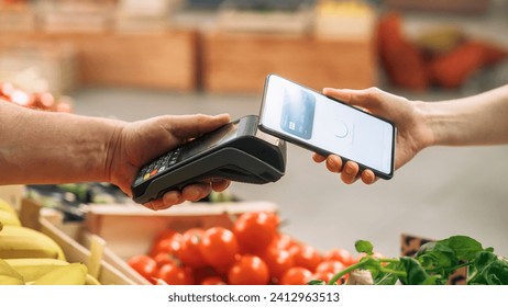 Consumer Buying Organically Sourced Farm Produce Using a Digital Credit Card to Pay with a Smartphone Software Through Contactless Online NFC Technology on a Bank Point-Of-Sale Terminal - Powered by Shutterstock