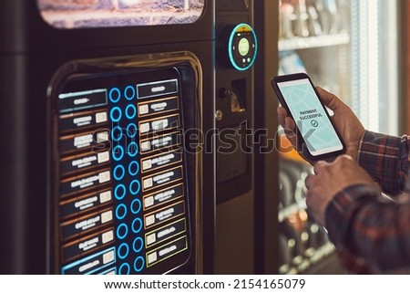 Consumer paying for product at vending machine using contactless method of payment with mobile phone. Man using payment app on smartphone to buy product. Male hand holding smart phone with payment app