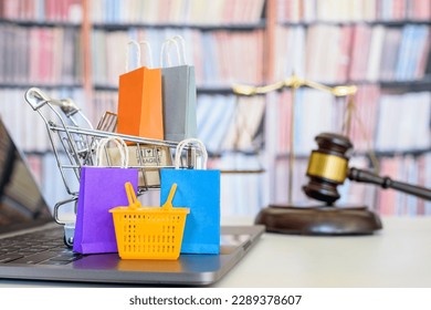 Consumer rights and consumer protection, business law concept : Shopping basket, shopping bags and  a shopping cart on a laptop computer with judge gavel, balance sale of justice and bookshelf behind.