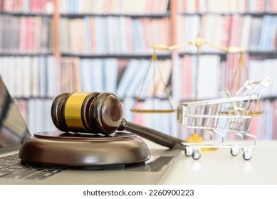 Consumer rights and protection, e-commerce law concept : Wooden judge's gavel rests on a laptop computer with a shopping cart and a balance scale of justice behind, symbols of fairness and commerce.