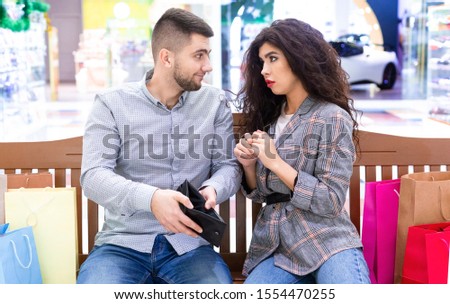 Consumerism concept. Woman asking to buy clothes, man showing empty wallet to his girlfriend