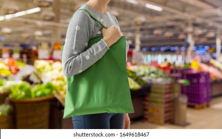 Consumerism And Eco Friendly Concept - Woman With Green Reusable Canvas Bag For Food Shopping Over Supermarket On Background