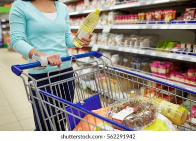 Consumerism, Food And People Concept - Woman With Shopping Cart Buying Vegetable Oil At Grocery Store Or Supermarket