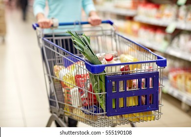 consumerism and people concept - woman with shopping cart or trolley buying food at grocery store or supermarket