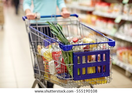 consumerism and people concept - woman with shopping cart or trolley buying food at grocery store or supermarket
