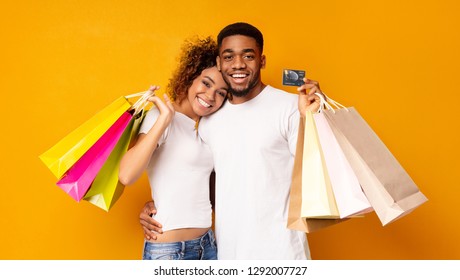 Consumerism And Relationship Concept. Happy Black Couple With Shopping Bags And Credit Card, Orange Background, Panorama