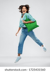 Consumerism, Sustainability And People Concept - Portrait Of Happy Smiling Young Woman In Turquoise Shirt And Jeans Walking With Green Reusable Canvas Bag For Food Shopping Over Grey Background