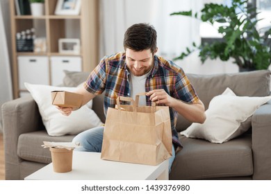 consumption, eating and people concept - smiling man unpacking takeaway food at home
