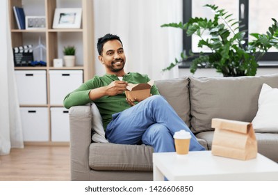 consumption and people concept - smiling indian man eating takeaway food at home