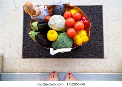 Contacless Food Delivery Service Concept. Top View At Bag With Grocery And Vegetables In Bag Delivered To Doorstep And Left. Online Shopping. Woman Picking Up Parcel At Entrance At Home. 