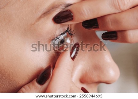 Contact lens application process. Closeup of an eye with a contact lens. Woman preparing lens with cleaning solution. Eyecare routine with lens on fingertip background.
