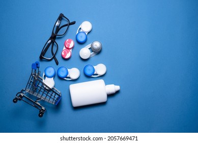 Contact Lenses, Eye Glasses And Eye Solution Bottle In The Shopping Cart On The Blue Flat Lay Background.