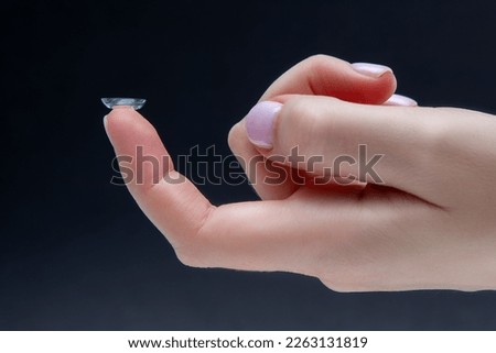 Contact lenses on a female finger on a dark background, close-up. A woman inserts a soft contact lens into her eye. Shallow depth of field