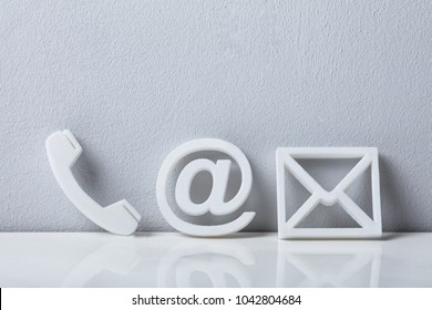 Contact Methods. Close-up Of A Phone, Email and Post Icons Leaning On White Wall
