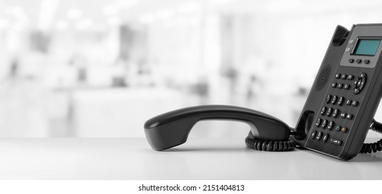 contact us. telephone devices at office desk for customer service support with B2B service technology concept. telephone with VOIP. black office voip phone with handset up on table on blurred office