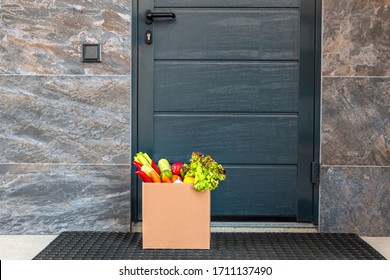 Contactless Delivery During A Pandemic Flu. A Box Of Fresh Vegetables And Fruits From A Supermarket Stands At The Front Door. Stay Home. Coronavirus. Quarantine.