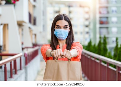 Contactless Delivery Of Goods During Covid 19, Coronavirus Pandemic. The Food Delivery Courier Is Holding A Large Paper Bag In Her Hands. Woman With Medical Mask Delivering Food.