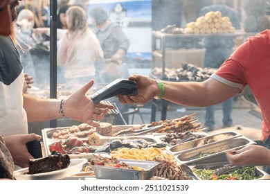 contactless payment transaction at an outdoor food stall. customer holds a payment terminal while another person prepares to tap their card.scene captures a modern and cashless payment method.  - Powered by Shutterstock