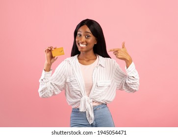 Contactless shopping concept. Joyful black woman pointing at credit card with smile on pink studio background. Portrait of charming African American lady recommending bank services