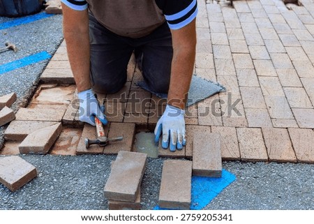 Contactor is kneeling on ground while placing bricks in pattern for walkway pavement repair