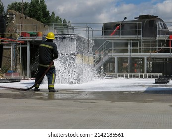 Container Fire Fighting Training. Fire Fighter Spraying Non Aspirated Foam Blanket On Smoldering Mock-up Container.