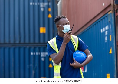 Container Man Worker Talking On Walkie-talkie To Colleague At Container Warehouse. African American Energy Engineering Specialist Wearing Protection Face Mask 