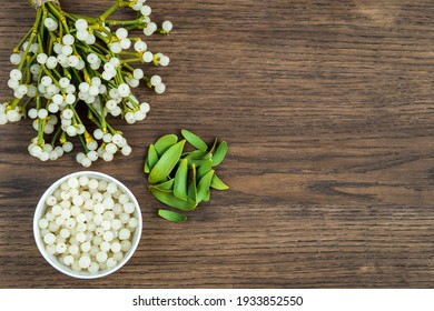 container with mistletoe fruit and branches of evergreen white mistletoe on a wooden surface, top view