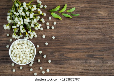 container with mistletoe fruit and branches of evergreen white mistletoe on a wooden surface, top view