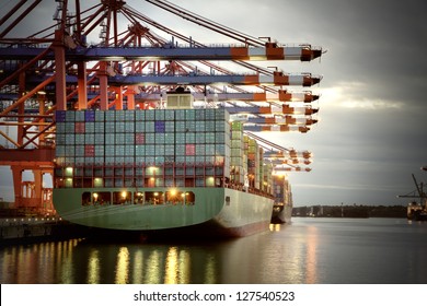 Container Ship In The Harbor Of Hamburg, Night Shot. Cloudy Sky.