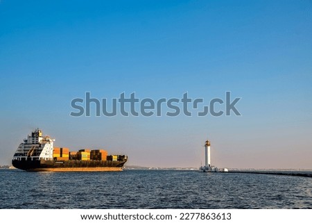 A container ship leaves the port near the lighthouse. Evening