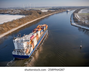 Container ship navigating through the Kiel Canal in winter conditions. Vessel, loaded with shipping containers, moves through the waterway.