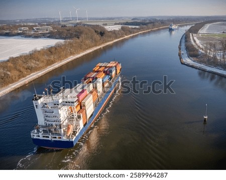 Container ship navigating through the Kiel Canal in winter conditions. Vessel, loaded with shipping containers, moves through the waterway.