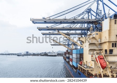 Container ship seen from the stern while berthed beneath giant gantry cranes at a container terminal in Cartagena, Colombia. The photograph highlights modern cargo handling equipment, commercial shipping, and international logistics.